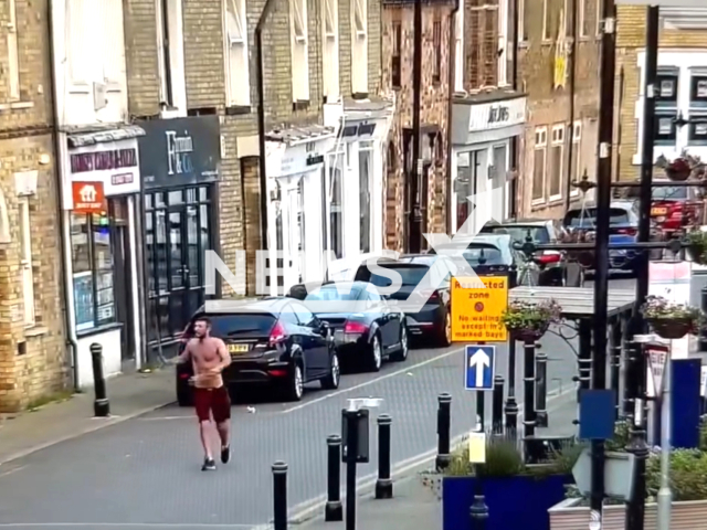 James Caulfield, 39, pulls a wooden pole from a flower bed and begins waving it down the street in Ramsey, UK. on June,16, 2024. Note: Picture is a screenshot from the video. (Cambridgeshire Constabulary/Clipzilla)