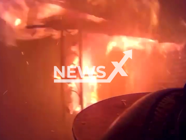 Firefighters putting out a vacant house on fire, with flames through the roof and someone possibly trapped inside, in Muskegon Heights, Michigan, USA. Note: Picture is a screenshot from the video. (Muskegon Heights Fire Dept)