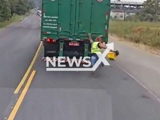This image is a screen grab of the video supplied titled NewsX-TruckHen-01.mp4: Dashcam shows a man hanging from a moving truck, slipping and narrowly avoiding being run over in Vale do Itajai, Santa Catarina, Brazil on Thursday, May 8, 2025.(Clipzilla/NX)