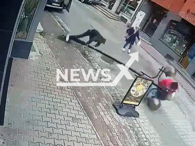 This image is a screen grab of the video supplied titled NewsX-PostsDrunk-01.mp4: CCTV shows a man trying to lean against a street lamp when it suddenly falls over and hits a woman passing by in Nowy Targ, Poland on Thursday, May 15, 2025.(Clipzilla/NX)