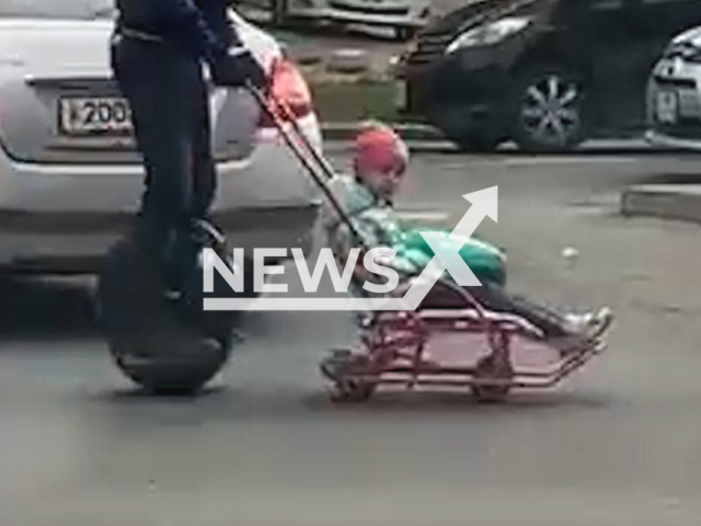 This image is a screen grab of the video supplied titled NewsX-UnicyclePush-01.mp4: Footage shows a man riding a unicycle and pulling a child on a sled in Irkutsk, Russia. The Russian Interior Ministry shared the video as a warning against unsafe transportation methods on Tuesday, May 20, 2025.(Clipzilla/NX)