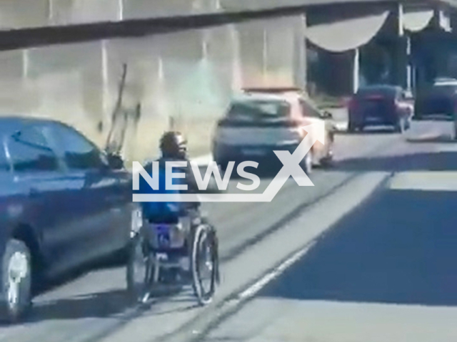 This image is a screen grab of the video supplied titled NewsX-WeyDis-01.mp4: A man in a wheelchair riding in the middle of traffic on a busy road in Niteroi in the Rio Metropolitan Region, Brazil, undated. The video was shared and went viral on social media on Tuesday, May 20, 2025. Police are working to enforce a council warning against using wheelchairs on public roads, citing safety risks to users and others.(Clipzilla/NX)