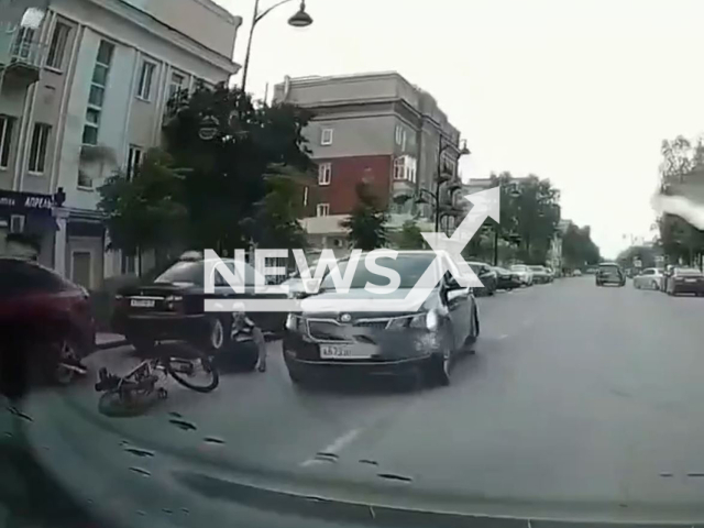 This image is a screen grab of the video supplied titled NewsX-RoadwayCyclist-01.mp4: The video shows a cyclist crashing into a parked car on the side of the road and almost ending up under a vehicle driving down the street in Murom, Vladimir Oblast, Russia on Thursday, June 19, 2025.(Clipzilla/NX)