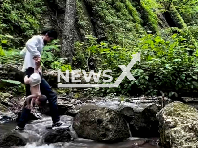 This image is a screen grab of the video supplied titled NewsX-BathingBaby-01.mp4: Footage shows father holding child only by the leg, carries him upside down across a bridge and plunges him into cold mountain water in Ingushetia, Russia, undated. footage shared on Instagram on Wednesday, July 16, 2025.(Clipzilla/NX)