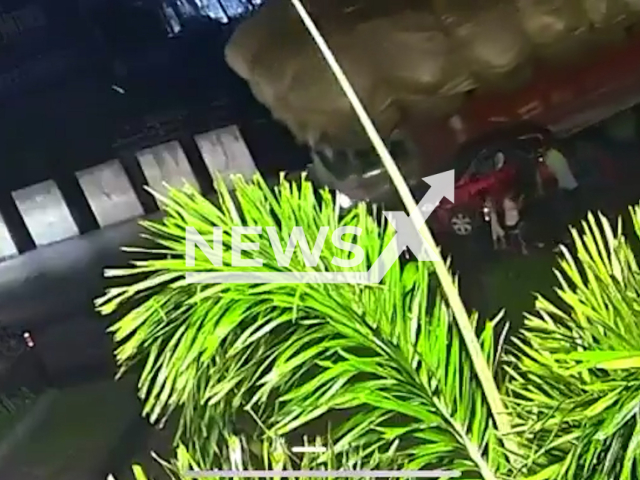 This image is a screen grab of the video supplied titled NewsX-HayTruck-01.mp4: CCTV footage shows a hay-loaded truck tipping over after an axle broke and crushing a car, moments after its occupants stepped out and narrowly escaped in Pilibhit district, Uttar Pradesh, India on Sunday,  Aug 31, 2025.(Clipzilla/NX)