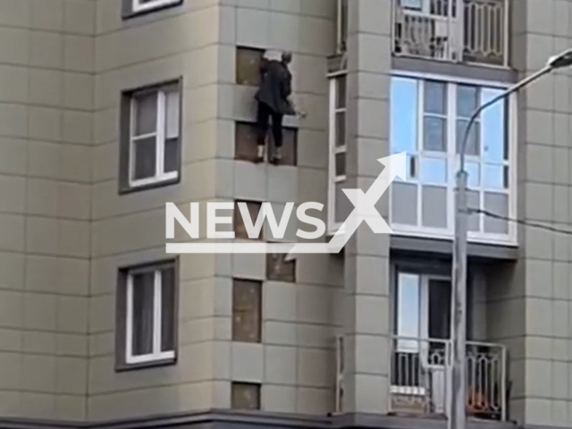 This image is a screen grab of the video supplied titled NewsX-BalconySlavyanka-01.mp4: Footage shows stunned residents watching a man use a tool to chip handholds and climb the facade of a apartment building in an extreme apology attempt on Rostovskaya Street, Slavyanka, St. Petersburg, Russia on Saturday, Sep. 27, 2025.(Clipzilla/NX)