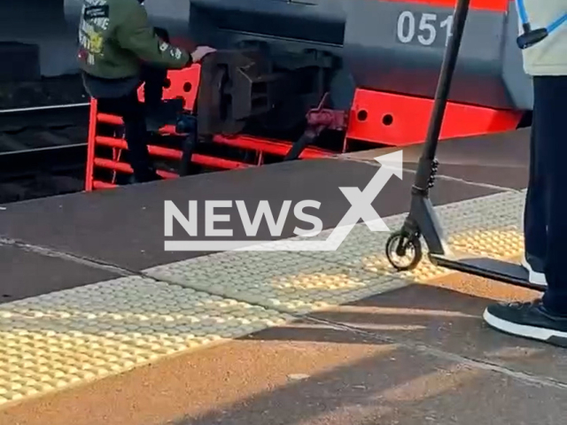 This image is a screen grab of the video supplied titled NewsX-RedTrainRide-01.mp4: Footage captures a masked train surfer clinging to the back of a moving train as it departs Leninsky Prospekt station in Saint Petersburg, Russia, undated. Footage shared on VKontakte on Wednesday, Oct. 1, 2025.(Clipzilla/NX)