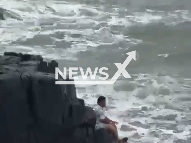 Sahas Ashpak Masali, 33, sits on rock before he is swept away by waves at Baga Beach in Goa, India. Authorities later confirmed his death. Note: Photo is a screenshot from a video. (Newsflash/NX)