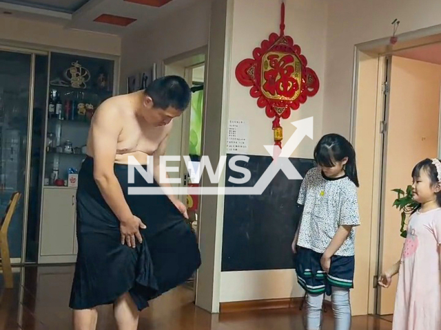 Father puts on skirt to teach daughters how to wear it in Linyi, China. Note: Picture is a screenshot from a video (1094818849s/AsiaWire)