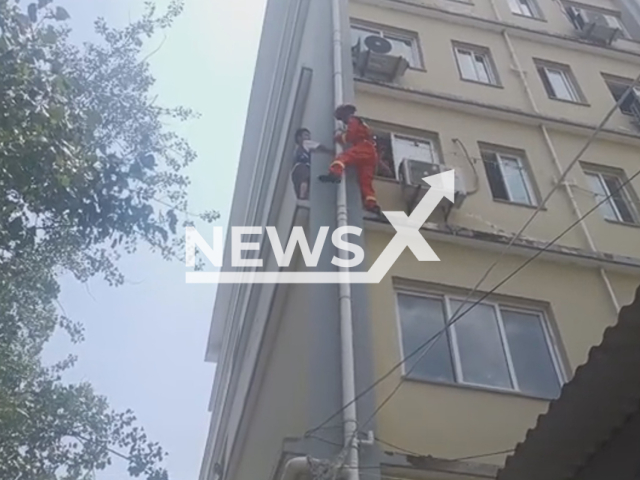 A fireman saves a boy who was stuck on the outer wall of a building window in Xinyang city, Henan province, China, on Thursday, August 4, 2022. The window is at a height of 10 meters. Note: Picture is a screenshot from a video (Xinyang Fire/AsiaWire)