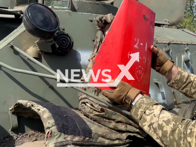 Ukrainian soldier holds inner part of Russian bulletproof vest near MT-LB armored fighting vehicle in Ukraine in an undated photo. Fighters of the 95th separate amphibious assault brigade cut up Russian bulletproof vests and saw ordinary iron plates that could not protect against a bullet. Note: This picture is a screenshot from the video (@Kochevenko/Newsflash).