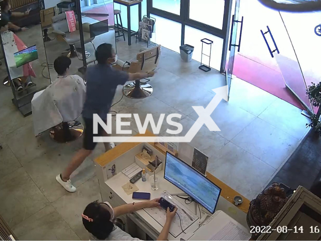 A barber rushes to catch the store's glass door before it collapses in Xi'an city, Shaanxi province, China, on Sunday, Aug. 14, 2022. He successfully saved the door from falling to the floor. Note: This picture is a screenshot from the video (205661831/AsiaWire).