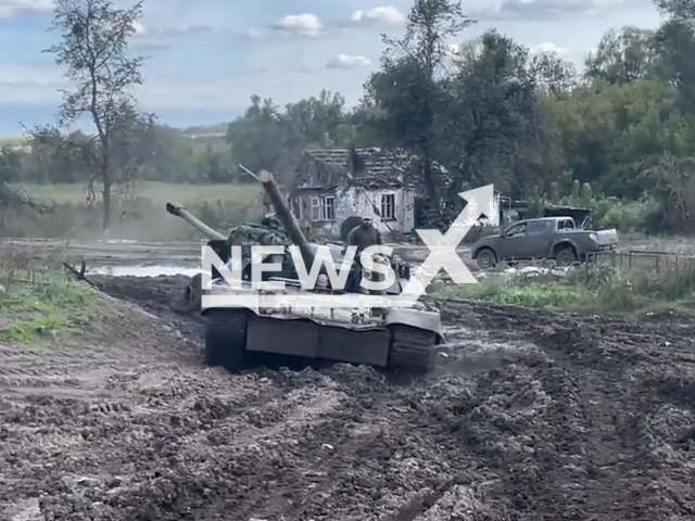 Ukrainian soldiers stand on tank going down the road in destroyed residential area in Ukraine in undated photo. Ukrainian soldier drove previously captured Russian T80U tank and pulled a captured Russian MSTA-B howitzer. Note: Photo is a screenshot from a video.(@AFUStratCom/Newsflash)