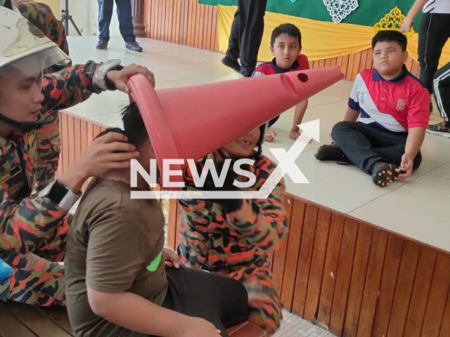 Firefighters attempt to free a boy whose head is stuck in a cone, in Pontian, in Johor, Malaysia, undated. According to the Fire Brigade, they spent about 20 minutes trying to free the boy. Note: Photo from Fire Brigade. (@bombajdt/Newsflash )