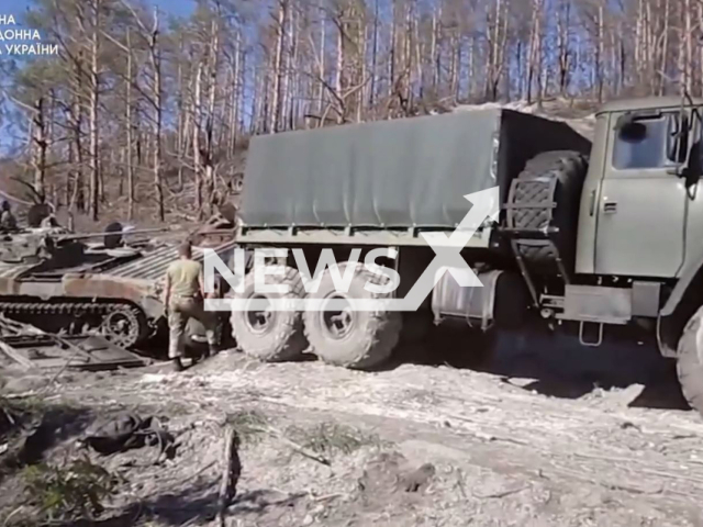 Ukrainian soldier stands near Ukrainian military vehicle and Russian tank tied to it in the Sviatohirsk direction of Ukraine in undated photo. The engineering unit of the State Border Service of Ukraine evacuated captured Russian BTR-82 and BMP-2. Note: Photo is a screenshot from a video.(@DPSUkraine/Newsflash)