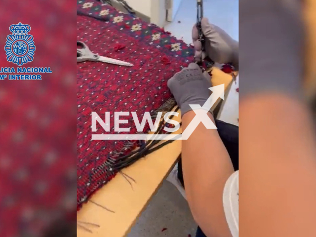 Police officer investigates a carpet with nine kilos of heroin between the fibers, undated. Two people were arrested at a bus station when dogs trained to find drugs found the heroin  in Barcelona, Spain. Note: Picture is a screenshot from a video (Newsflash)