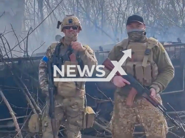 Volunteers from the United States pose against the backdrop of a destroyed Russian tank in the village Lukyanovka on the border of Kyiv and Chernihiv regions in Ukraine. Note: Picture is a screenshot from a video (@UkrainianLandForces/Newsflash)