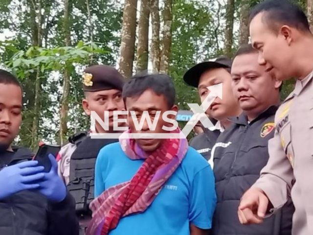 Picture shows the money-multiplying shaman named Tohari, alias Mbah Slamet, (blueshirt) with police,  undated. Police found 12 bodies of people he allegedly killed   near his home and speculate there may be more victims  in Banjarnegara , Indonesia. 
  
 Note: Photo is a screenshot from a video. (Newsflash)